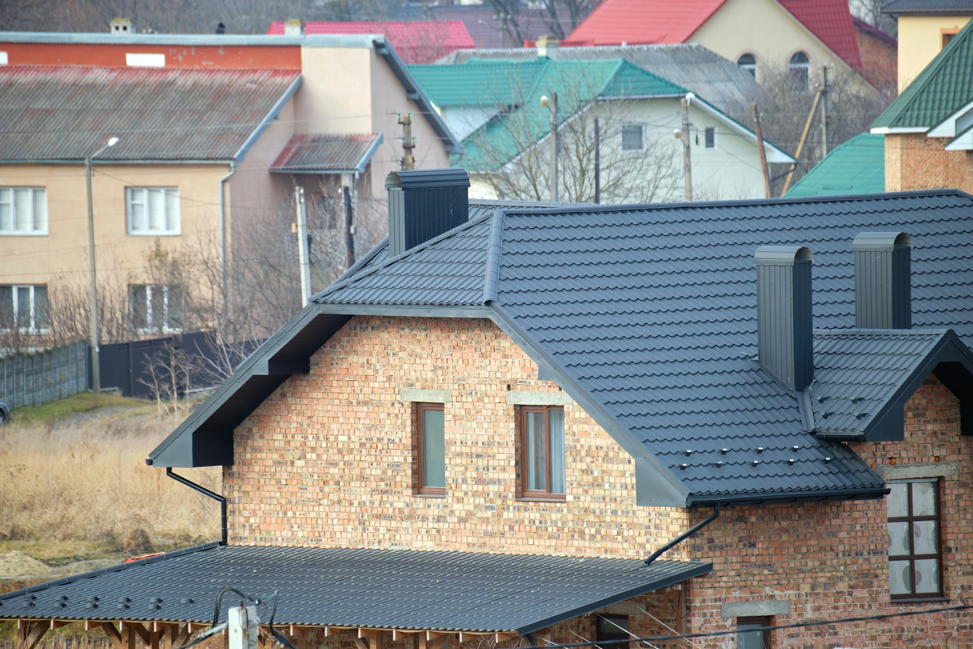 Chimney on house roof top covered with metallic shingles under construction. Tiled covering of